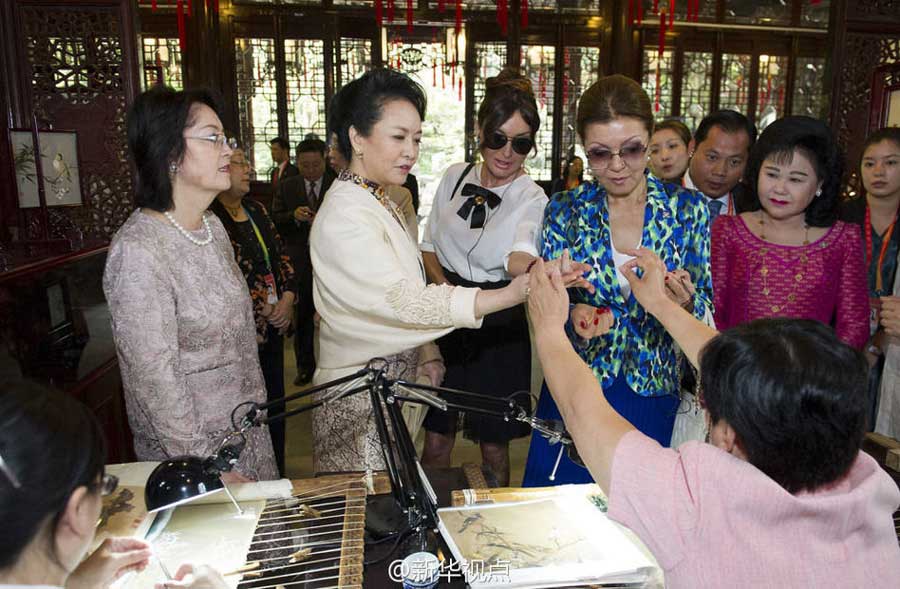 Su Huiping, a Shanghai embroidery artist, puts a nearly invisible silk thread through the tiny eye of a needle as Chinese first lady Peng Liyuan (second from left) and her counterparts watch at the Yuyuan Garden in Shanghai on Wednesday.[Photo/Xinhua]