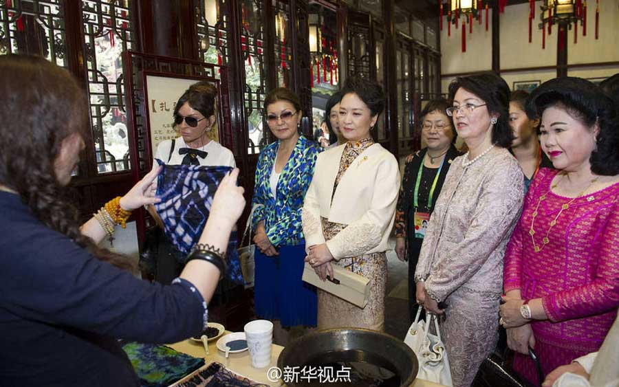 An artist demonstrates a creation of tie-dye, which turns cotton cloth into colorful pieces with the help of different herbal plants, as Chinese first lady Peng Liyuan (3rd from right) and her counterparts watch at the Yuyuan Garden in Shanghai on Wednesday.[Photo/Xinhua]