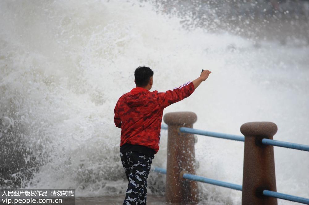 Tourists take risky photos with giant waves in Qingdao