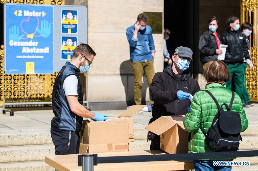 Staff members offer face masks to people in front of City Hall of Dresden, Germany