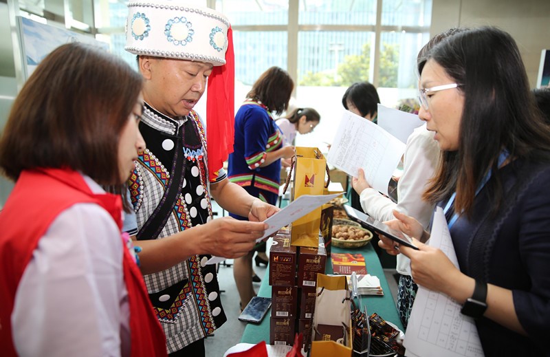 A businessman from Nujiang Lisu autonomous prefecture, southwest China’s Yunnan province, introduces agricultural products for poverty alleviation to an employee of the Shanghai branch of the Agricultural Bank of China, in Huangpu district, Shanghai, June 24. (People’s Daily Online/ Liang Zhiqiang)  