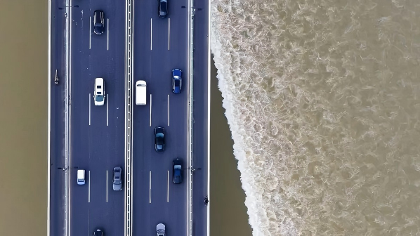 Vehicles stream across Jiubao Bridge as Qiantang River tides roll below