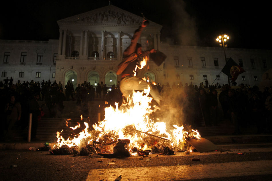 Demonstrators protesting against the new 2013 state budget walk past a fire burning in front of the parliament in Lisbon, Portugal on October 29, 2012. (Xinhua/AP)