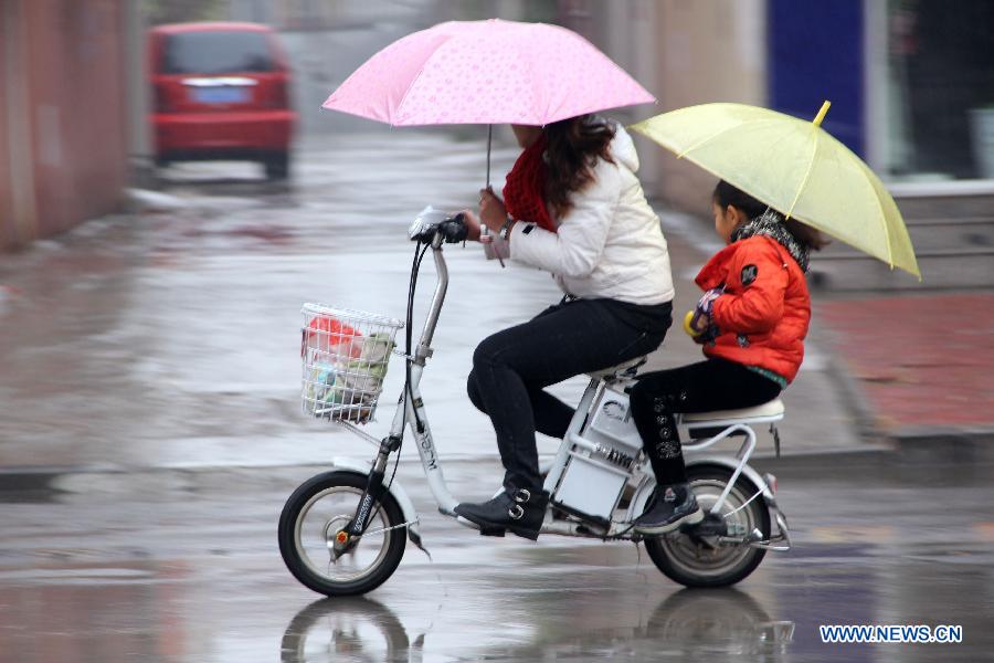 A woman rides an electric bicycle with a girl in the rain in Neihuang County of Anyang City, central China's Henan Province, Nov. 10, 2012. A strong cold snap has brought rainfall and wind to many parts of northern China since Friday night, causing a fall in temperature and scattered snowfall in the following days. (Xinhua/Liu Xiaokun)