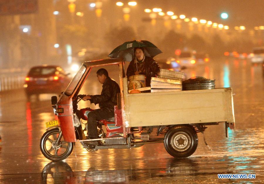 Citizens ride a motor tricycle in the rain on Beima Road of Yantai City, east China's Shandong Province, Nov. 10, 2012. A strong cold snap brought rainfall and wind to the coastal city, causing a fall in temperature. (Xinhua/Shen Jizhong)