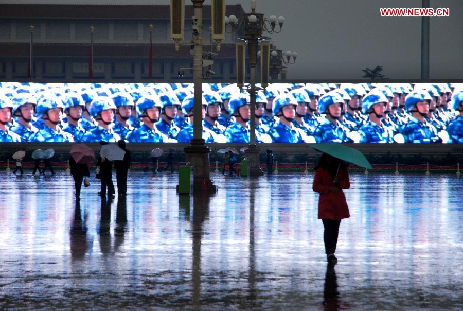 Tourists walk in front of a large electronic board amid rain at the Tian'anmen Square in Beijing, capital of China, Nov. 10, 2012. (Xinhua/Li Gang) 