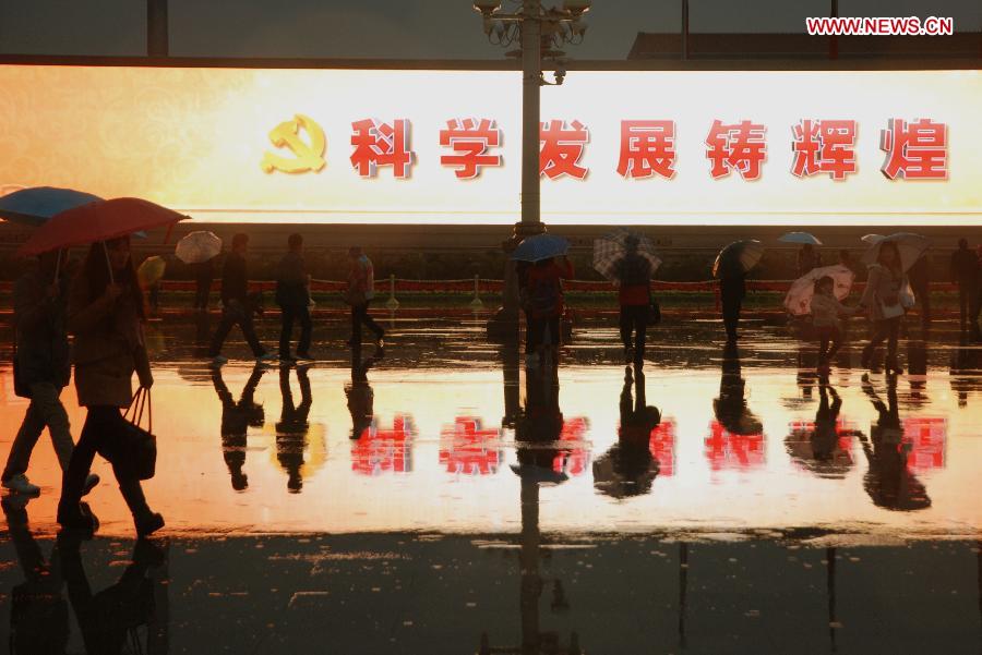 Tourists walk in front of a large electronic board amid rain at the Tian'anmen Square in Beijing, capital of China, Nov. 10, 2012. (Xinhua/Li Gang) 