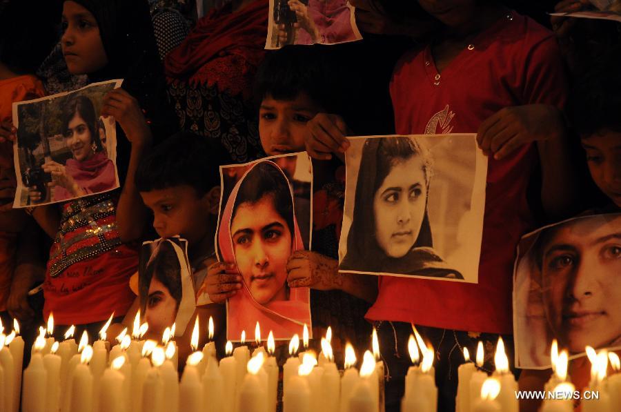 Children hold photos of Pakistan's child activist Malala Yousafzai as they stand alongside burning candles during a ceremony to mark "Malala Day" in Karachi, Pakistan, Nov. 10, 2012. (Xinhua/Masroor)