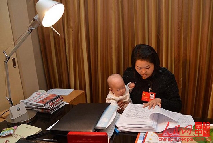 Luo Wei, a deputy to the 18th National Congress of the Communist Party of China, reads material while taking care of her five-month-old daughter in a hotel in Beijing on Nov 10, 2012. (Photo/ People’s Daily Online)
