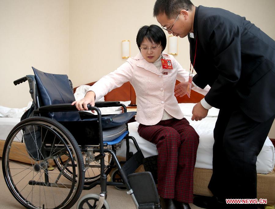 Hou Jingjing, a delegate to the 18th National Congress of the Communist Party of China (CPC), is helped by her husband Xiang Huali to sit on wheelchair at a hotel room in Beijing, capital of China, Nov. 11, 2012. (Xinhua/Chen Jianli)