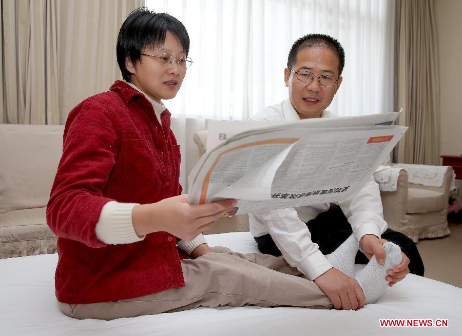 Hou Jingjing, a delegate to the 18th National Congress of the Communist Party of China (CPC), reads newspaper while her husband Xiang Huali massages her paralyzed legs at a hotel room in Beijing, capital of China, Nov. 11, 2012.(Xinhua/Chen Jianli)