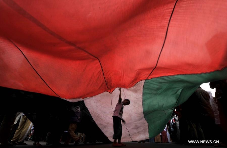 A boy stands under a huge Palestinian flag during a protest against Israeli air strikes on Gaza, in Jakarta, Indonesia, Nov. 18, 2012. (Xinhua/Agung Kuncahya B.) 