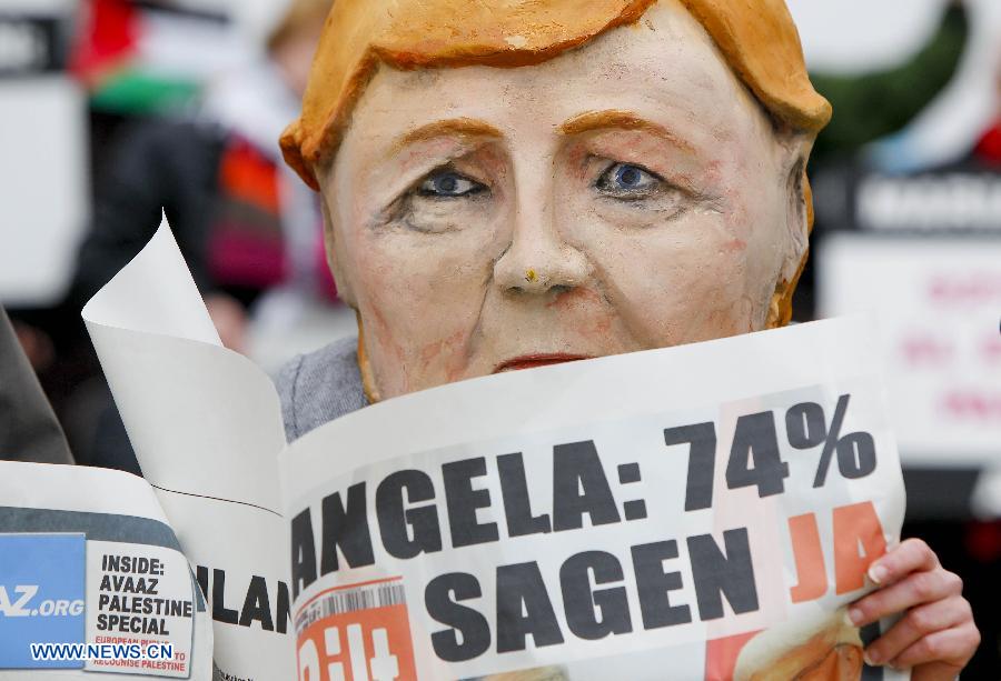 An activist wearing giant heads of German Chancellor Angela attends a rally in front of EU headquarters in Brussels, Belgium, Nov. 19, 2012. Demonstrators installed the giant flag to urge EU backing the Palestinian membership in the United Nations. (Xinhua/Zhou Lei) 