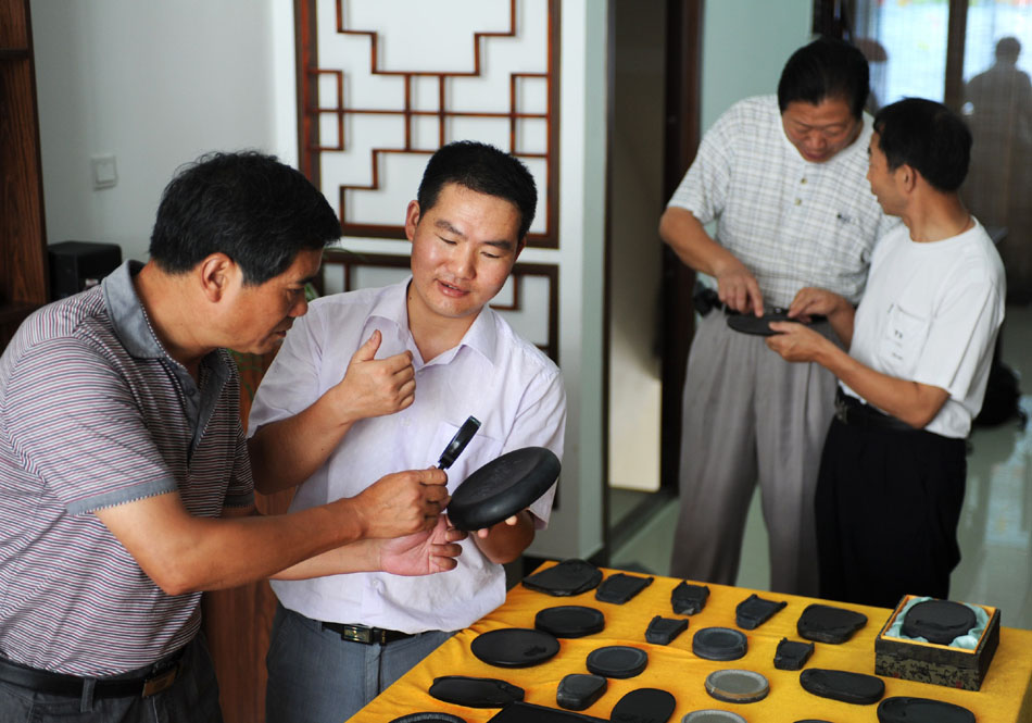 Wen Xin (2nd L) introduces his inkstone carvings to customers in Shexian County of east China's Anhui Province, Aug. 7, 2012. (Xinhua/Du Yu)
