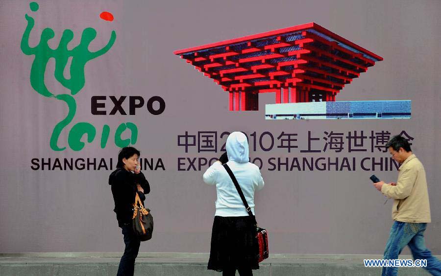 File photo taken on April 22, 2010 shows that visitors make phone calls and take photos by mobile phones in front of a poster of Shanghai World Expo. in east China's Shanghai. (Xinhua/Wang Song)