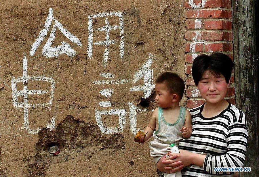 File photo taken on May 1, 1999 shows that a women carrying a baby stands near a spot for public telephone in Fudian Town of Ruyang County, central China's Henan Province. (Xinhua/Wang Song)
