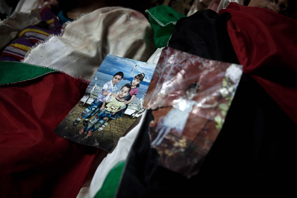 Two photos of children are placed on dead bodies of their parents in a hospital in the Gaza Strip on Nov. 19, 2012. (Xinhua/Chen Xu)