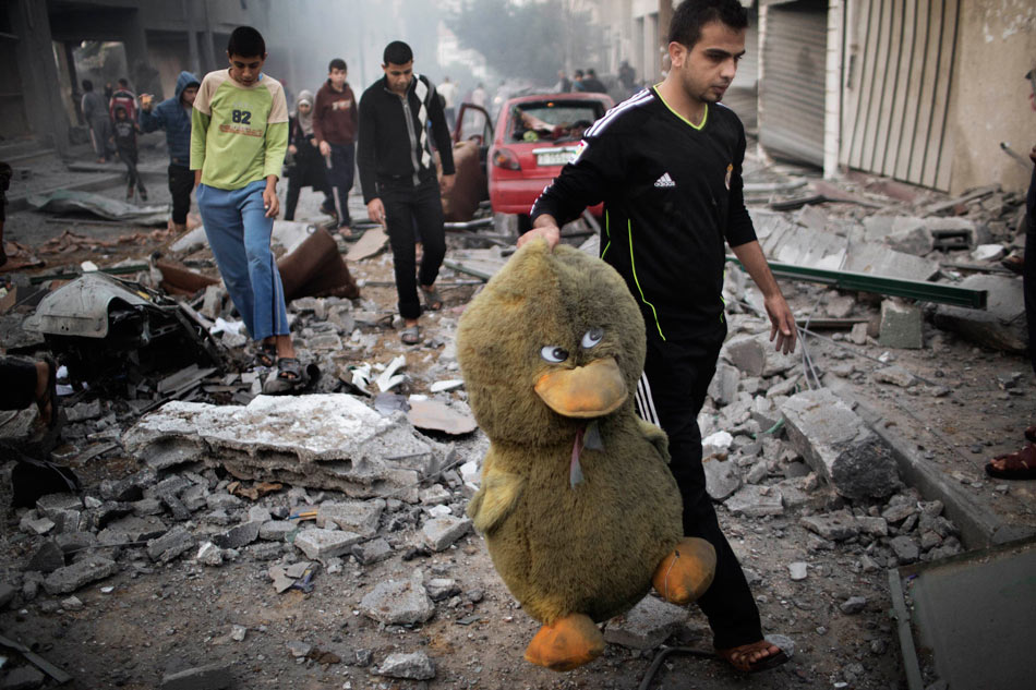 A Palestinian picks up a toy from the ruins of buildings destroyed by Israeli air strikes in Gaza City, on Nov. 19, 2012. (Xinhua/AFP)