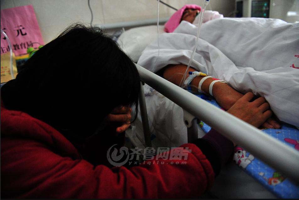 Gong Yuben’s mother cries beside her son’s bed, tightly holding on the boy’s hand. (iqilu.com/Zhang Xiaobo)