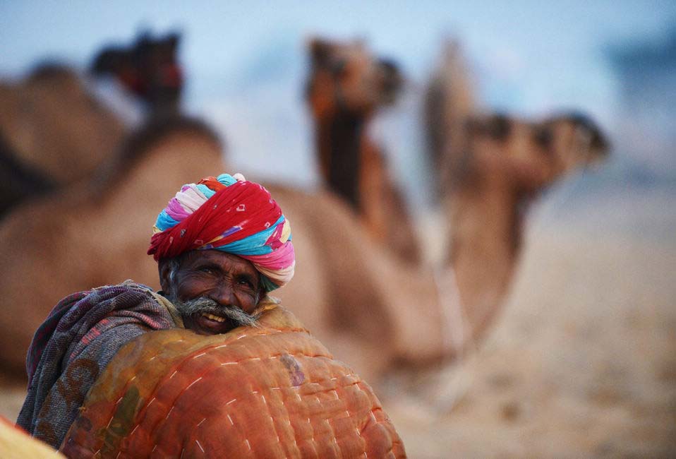 A camel trader keeps warm with a blanket at dawn as he sits near a herd of camels at the annual Pushkar Fair in Rajasthan, India on Nov.21, 2012.(Xinhua/AFP)