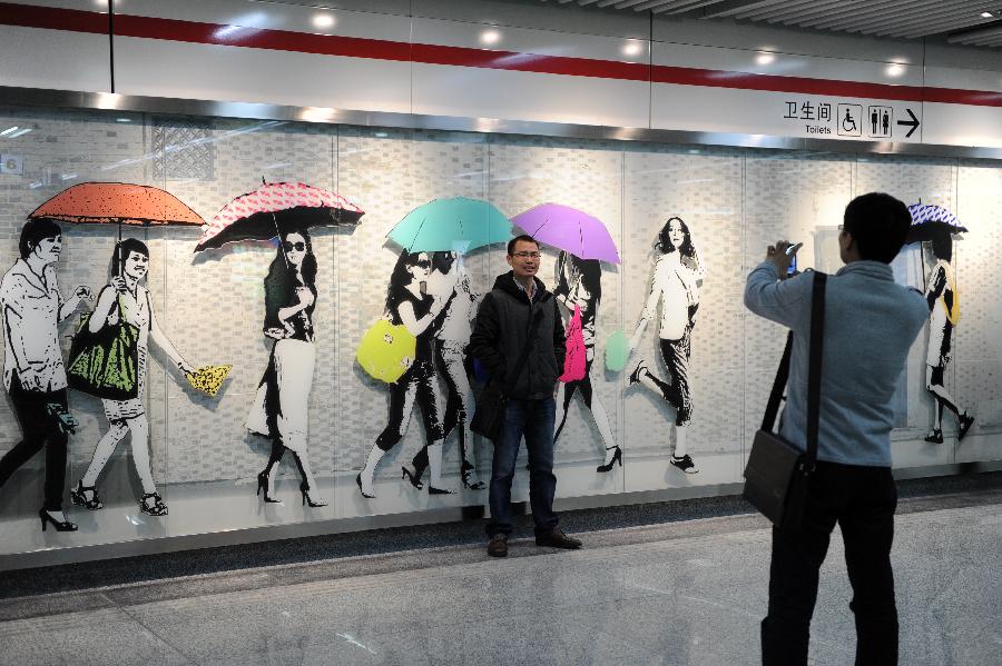 A man poses for photo in front of an art wall inside the Fengqilu Station of the Hangzhou Subway Line 1 in Hangzhou, capital of east China's Zhejiang Province, Nov. 24, 2012. Among the 31 stations of the Hangzhou Subway Line 1 which started a trial operation on Saturday, 11 stations were decorated with distinctive art designs. (Xinhua/Ju Huanzong) 