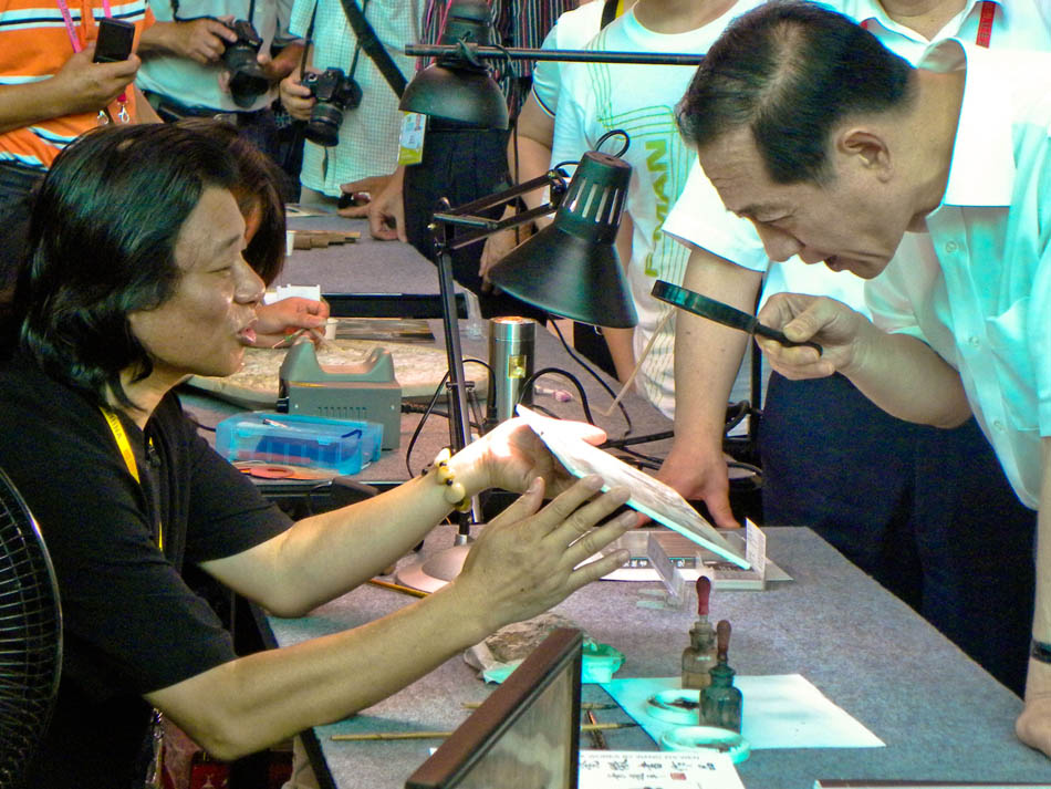 Wang Zhiwen (L) shows one of his miniature calligraphic creations to visitors at the World Expo Park in Shanghai, east China, July 29, 2010. (Xinhua/Ke Zhixiong)