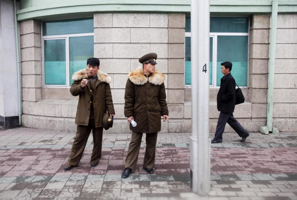 Two soldiers smoke cigarettes as a pedestrian walks past on a street in Pyongyang. (Photo/Xinhua)