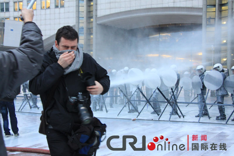 A journalist covers his face after tear gas is used by the riot police to disperse the crowd during a protest against E.U. agricultural policies at the Place du Luxembourg, outside the European Parliament in Brussels, Belgium, Nov. 26, 2012. Dairy farmers from all over Europe demonstrated in Brussels on Monday to protest against falling milk prices caused by overproduction in the continent. (Photo/CRI Online)