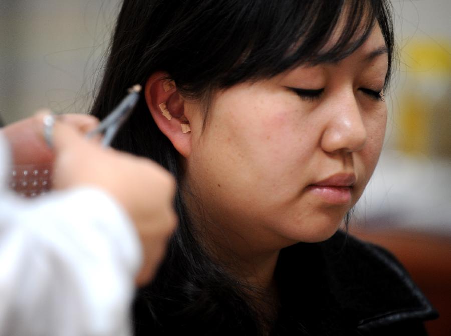A girl puts herbs paste on her ears in the Shanxi College of Chinese Traditional Medicine Subsidiary Hospital in Taiyuan, capital of north China's Shanxi Province, Nov. 23, 2012. More and more Chinese are disposed to preventive treatment of discease rather than curative treatment, they receive acupuncture, moxibustion, herbal paste or other Chinese traditional regimen to improve sub-healthy state.(Xinhua/Yan Yan) 