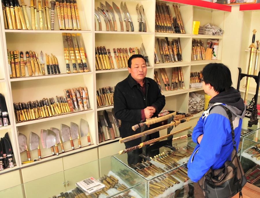 Ma Zizheng, a professional Bao'an broadsword maker, introduces Bao'an broadswords to a visitor at his store in Jishishan County, northwest China's Gansu Province, Nov. 29, 2012. (Xinhua/Huang Wenxin)  