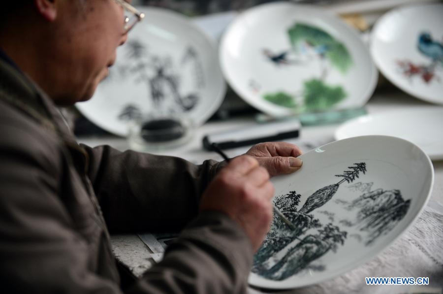 Bian Xiping, inheritor of intangible cultural heritage ceramic arts and crafts, paints on a ceramic plate by using traditional skills in Huating County, northwest China's Gansu Province, Nov. 29, 2012. 