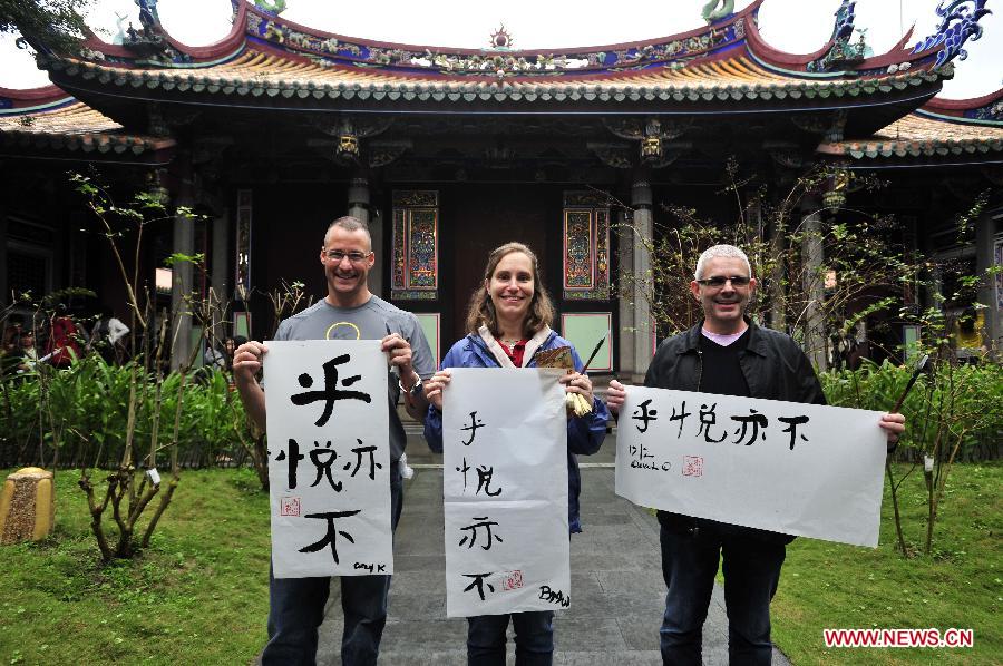 Tourists from Great Britain pose for pictures with their calligraphy works during a Chinese calligraphy experience activity at Taipei Confucius Temple in Taipei, southeast China's Taiwan Province, Dec. 2,2012. (Xinhua/Wu Ching-teng)