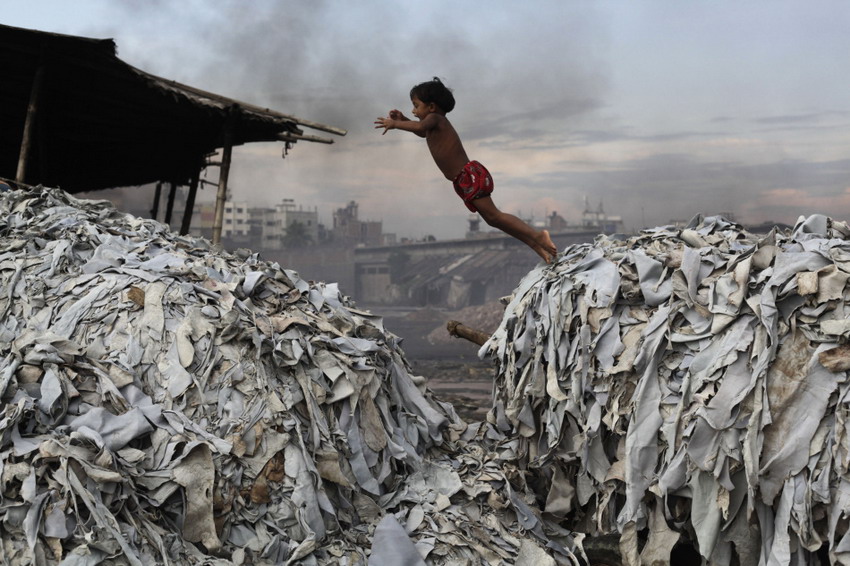 A child jumps on a pile of wastes used to produce poultry feed in Kada, Bengal on Oct 9, 2012. (Photo/Reuters)