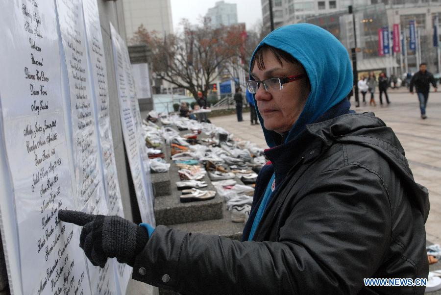 A woman reads names of deceased women at annual Shoe Memorial on the steps of Vancouver Art Gallery in Vancouver, Canada, Dec. 6, 2012. December 6th is Canada's National Day of Mourning for women who have met with violent deaths. Shoes in bags represent dead women, and those without bags represent women who are alive but suffer from abuse. (Xinhua/Sergei Bachlakov)