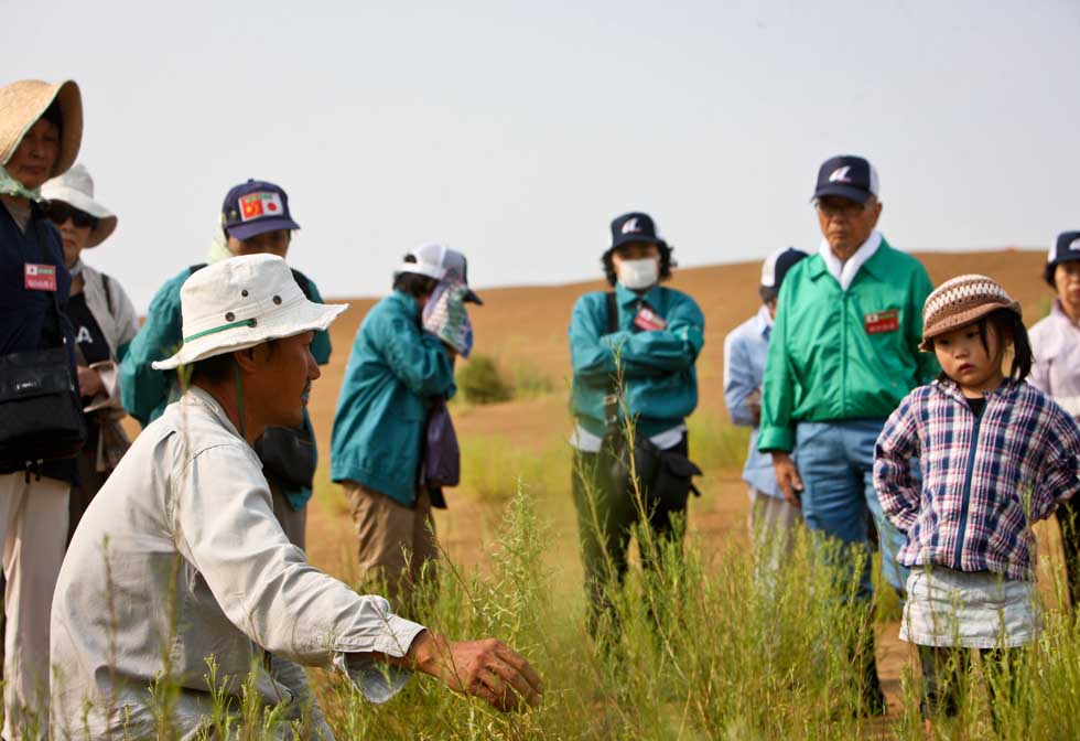 Mase Hiroki (L, front) introduces the condition of plants in desert to Japanese volunteers in Engebei, Ordos, north China's Inner Mongolia Autonomous Region, Aug. 26, 2012.(Xinhua/Xie Xiudong)