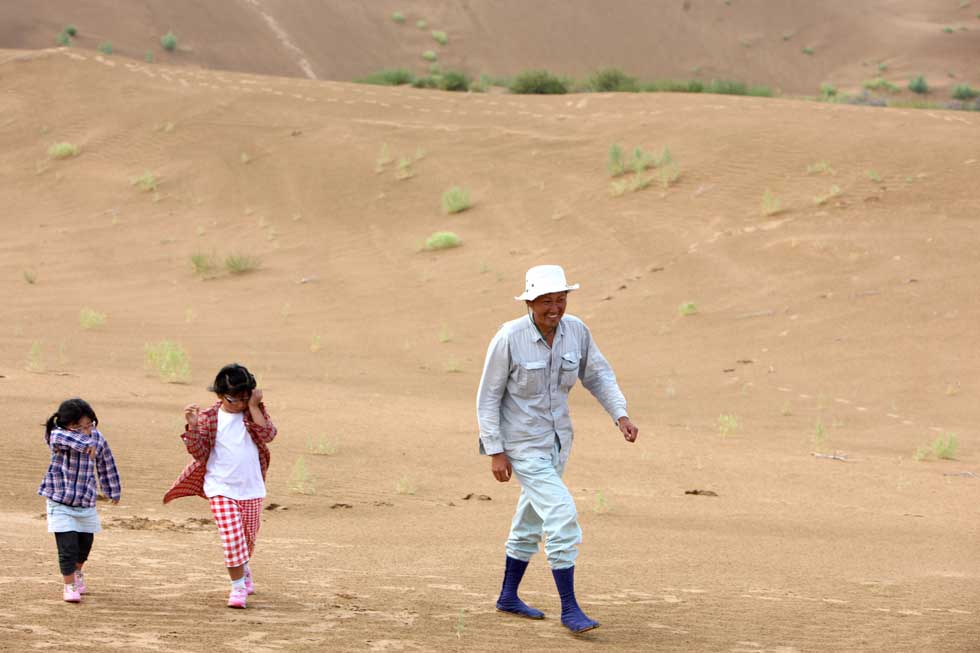 Mase Hiroki (R) walks with Ishimaru Tsuduna (2nd L) and Ishimaru Kokoro, who came with their mother as temporary volunteers to plant trees, in Engebei, Ordos, north China's Inner Mongolia Autonomous Region, Aug. 26, 2012.(Xinhua/Xie Xiudong)