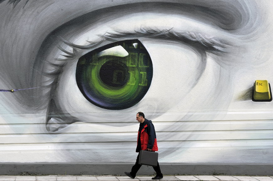 A man walks past a wall printed a large green eye in Athens, Greece on March 8, 2012. (AFP/Louisa Gouliamaki)