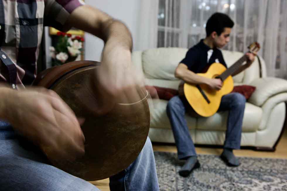Peyam plays a drum while his son Bai Yun plays guitar on the sofa at their home in Yinchuan, capital of northwest China's Ningxia Hui Autonomous Region, March 15, 2012.(Xinhua/Zheng Huansong)