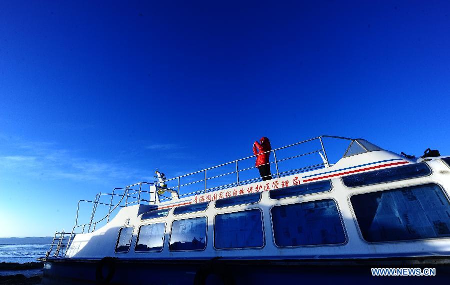 A tourist takes pictures on a boat at the scenic area of the Qinghai Lake in northwest China's Qinghai Province, Dec. 12, 2012. The Qinghai Lake, China's largest inland salt water lake, presents a beautiful scenery in winter. (Xinhua/Zhang Hongxiang)