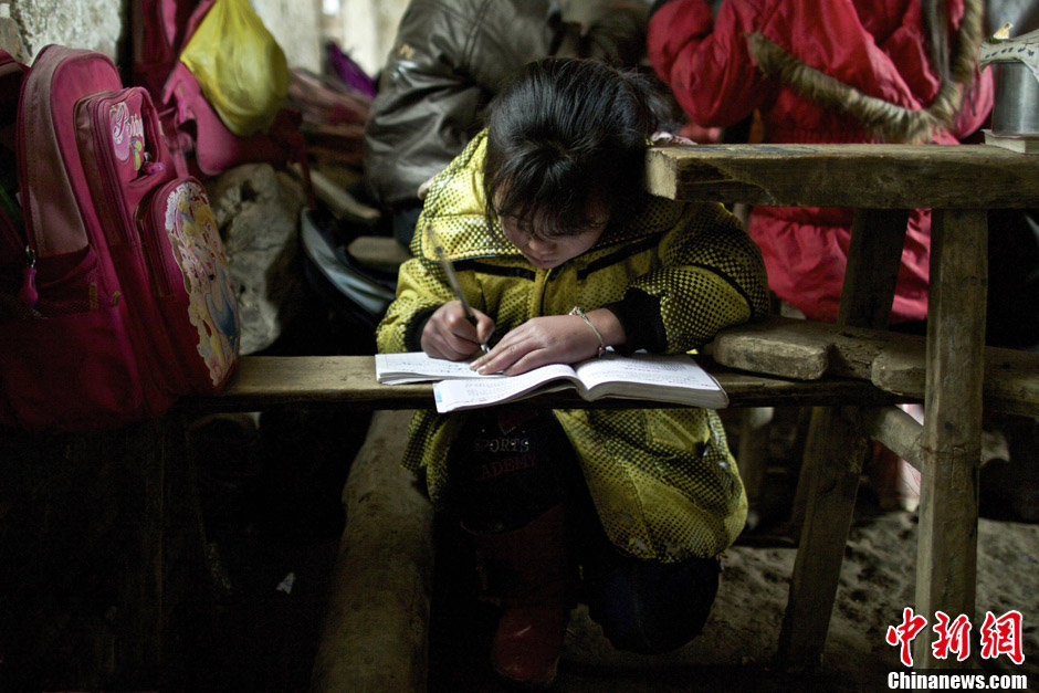 A child has to squat on the ground to read the book due to the poor lighting condition. Nishu primary school has only two old mud huts without electricity. (Chinanews/Feng Zhonghao) 
