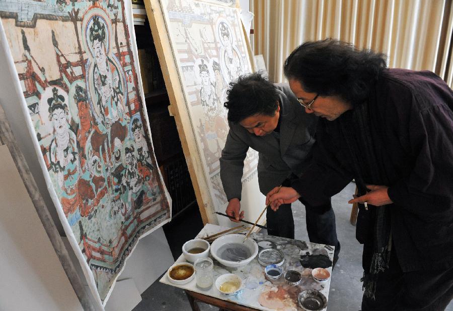 Teng Ting (R), the founder of a high temperature ceramic paints, and painter Shao Hongjiang from Dunhuang Academy work on a painting of the Grottoes together in Jingdezhen, east China's Jiangxi Province, Dec. 12, 2011.(Xinhua/Zhang Wu)