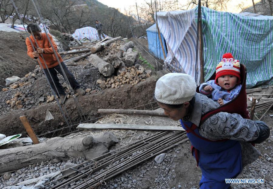 A granny carries a baby on the back as she walks past a construction site in Adu Village of Jiaokui Township in the earthquake-hit Yiliang County, southwest China's Yunnan Province, Dec. 13, 2012. (Xinhua/Lin Yiguang)