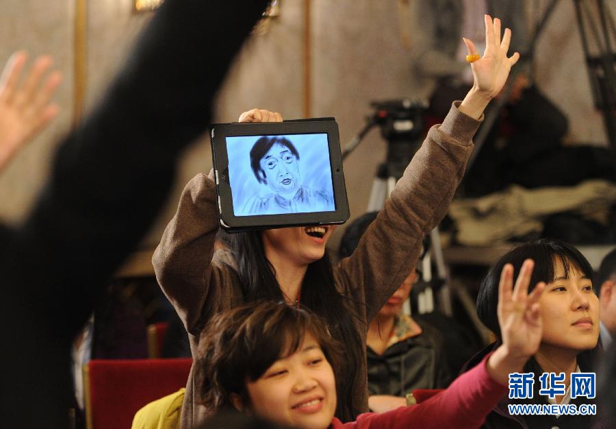 A reporter, holding a tablet PC painting the portrait of Feng Jicai hopes to get host's attention and obtain the opportunity of questioning. 