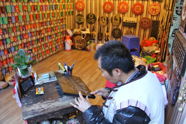 A craftsman carves a piece of wood in his store on a business street of Lijiang. (Photo: CRIENGLISH.com/Zhang Linruo)