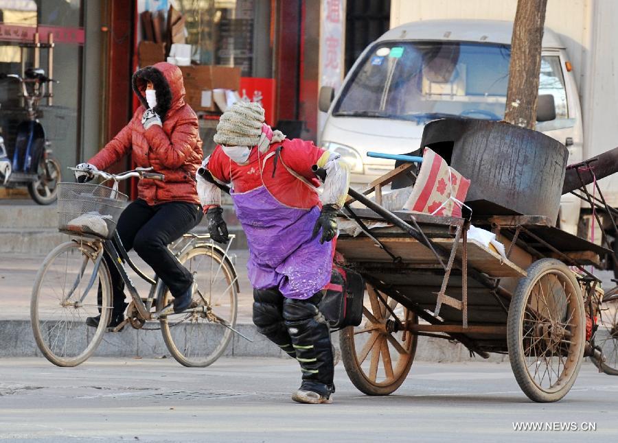 A woman pulls a handcart against chill wind in Baoding, north China's Hebei Province, Dec. 23, 2012. The provincial meteorological observatory issued a blue alert on cold wave on Saturday. Most parts of Hebei suffered from a sharp decline of temperatures and strong wind. (Xinhua/Zhu Xudong) 