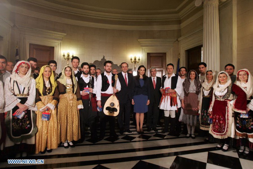 Greek Prime Minister Antonis Samaras (C) poses for photos with members of cultural clubs, dressed in traditional costumes, at Maximos Mansion, central Athens, Greece, Dec. 24, 2012. On Christmas Eve, traditional carols are sung throughout Greece, giving a tone of optimism in a country struck by the economic crisis. (Xinhua/Marios Lolos)
