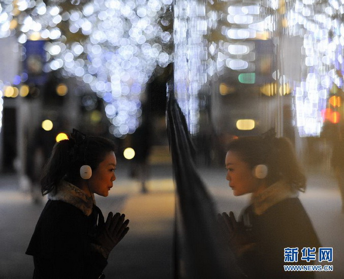 A pedestrian looks at inside of the window in the street with Christmas lighting in Toyko, Japan, Dec. 10, 2012. (Photo/Xinhua)