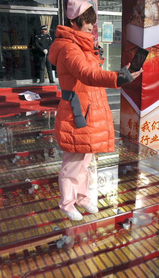 A citizen takes photos as she stands on the "gold road," on which 1,000 pieces of 1,000-gram gold bars are laid beneath toughened glass, in a gold shop in Binzhou City, east China's Shandong Province, Jan. 1, 2013. (Xinhua/Zhang Binbin)