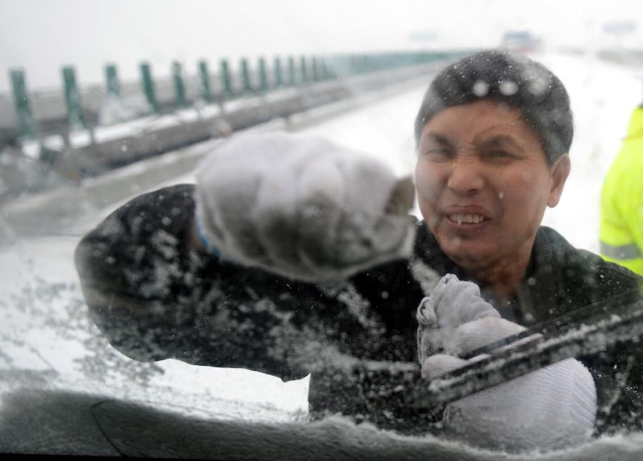 A driver tries to clean the snow on the windscreen of his vehicle stranded on the Nanchang-Zhangshu section of the Shanghai-Kunming highway in east China's Jiangxi Province, Jan. 4, 2013. Vehicles were blocked in a traffic jam on the highway for a couple of hours due to a heavy snowfall in Jiangxi on Friday. (Xinhua/Zhou Ke)