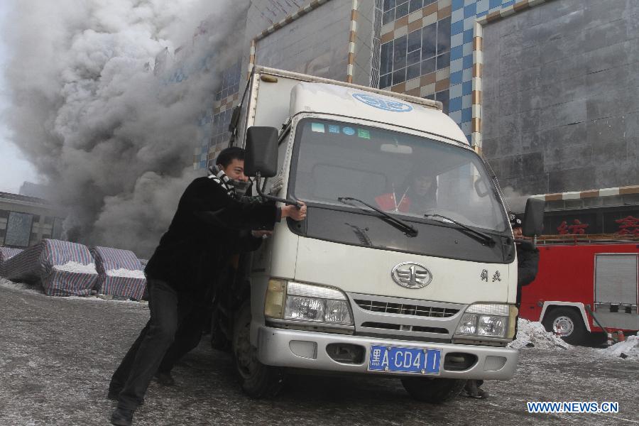 People push a truck away from a shopping mall in Harbin, capital of northeast China's Heilongjiang Province, Jan. 7, 2012. Casualty information is unknown yet after the fire started at around 9 a.m. (0100 GMT) in the Guorun Home Textiles Shopping Mall in downtown Harbin on Monday. The fire consumed an area of 9,400 square meters over the course of three and a half hours before being stopped. Firefighters helped evacuate shoppers from the five-story building. (Xinhua/Xiao Jinbiao) 